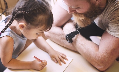 Father watches lovingly as his younger daughter writes or draws.