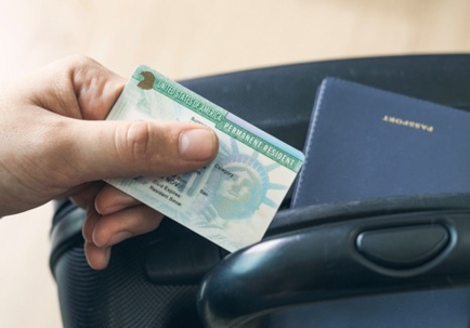 Man holding permanent resident (green) card. United States passport on suitcase