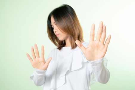 Woman holding both hands up with palms facing outward in a gesture of refusal or stopping, looking to the side against a light background.