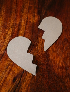 Two pieces of a broken heart shape made from paper lie separated on a wooden surface.