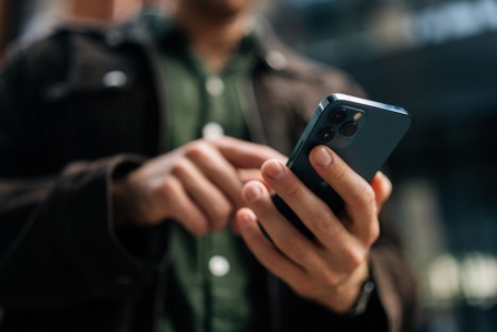 Close-up hands of unrecognizable man using smartphone standing on city street, posting on social media